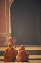Two woman sat talking in front of one of the red sand stone buildings that frame the Taj Mahal.
