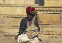 Musician with Sitar  sat on the ground outside a building.
