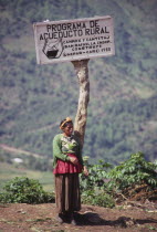 Indigenous woman standing below a sign describing a village water project  highlands.