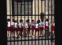 School children waiting in a line  viewed through window of a colonial building.