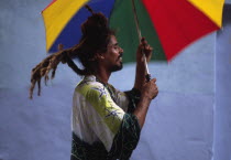 Rastafarian man on stilts  with umbrella as part of street parade