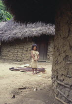Young Cogi girl holding cotton yarn  standing in-between two huts.