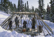 A group of people constructing a camp out of wood in the snow.