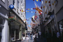 St Peter Port. View up narrow cobbled High Street  pedestrian shopping street with colourful flags attached to buildings.