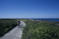 Vale. Cyclists riding on path next to Baie de Port Grat.