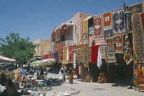 The souk with carpets displayed from walls and awnings of shopfronts opposite street vendors selling shoes  hats and woven basket.Market Marrakech