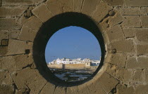 Fortified coastal town framed in circular opening in wall.