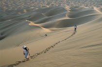 Tourists walking through desert landscape leaving trails of footprints across the dunes.