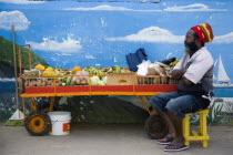 Fruit and vegetable stall holder in front of wall painting in Clifton