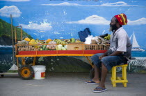 Fruit and vegetable stall holder in front of wall painting in Clifton