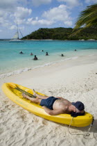 Man lying in kayak sunbathing on the beach of Petit Bateau