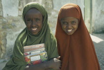 Portrait of two schoolgirls with covered heads carrying school books.