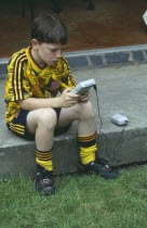 Young boy in a football kit playing a Nintendo Gameboy