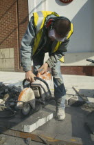 Workman cutting pavement slabs with angle grinder