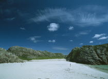 White Sand Beach with large moss covered bolders and a woman standing in the distance
