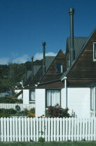 Line of houses with narrow chimneys and white painted picket fences.