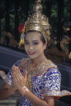 Female Temple dancer in traditional dress outside Grand Hyatt Erawan Hotel giving the traditional Thai Wai greeting