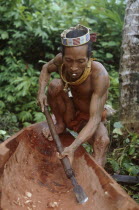 A Mentawi man hollowing out a canoe whilst he smokes a hand rolled cigarette