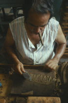 Man smoking a cigar whilst he rolls cigars in a cigar factory