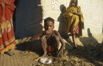 Boy in Ganges Plain village eating rice with his hands  little girl leaning against wall of building behind.