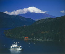 Mount Fuji with snow cap above the lake with a passenger boat passing the Hakone torii gate