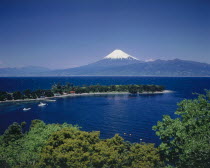 Mount Fuji with snow cap above the tree lined deep blue water of the bay