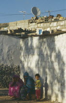 Women and child outside slum housing with satellite dish on the roof