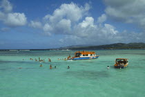 Nylon Pool with tourists swimming or standing in shallow water by boats