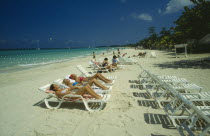 Female tourists beach sunbathing on sun loungers facing away from the water