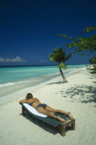 Woman Sunbathing on lounger on beach near sea and coconut palm tree