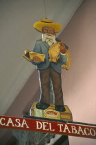 Sign hanging outside cigar shop showing bearded old man in hat holding cigars standing on a cigar box