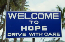 Blue and white roadsign outside village reading Welcome To Hope Drive With Care
