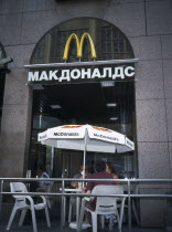 McDonalds Restaurant with people sitting at table and chairs with umbrella outside entrance with restaurant sign in Russian