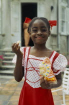 Young smiling girl in red and white dress with red ribbons in hair eating crisps from a packet