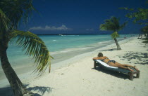 Woman sunbathing on lounger on beach near water and coconut palm trees