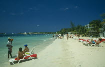 Man selling lobster to tourists on beach sitting on sun loungers by the water with other tourist sunbathing