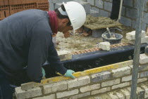Workman wearing a hard hat using a spirit level to lay reclaimed facing bricks
