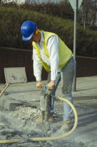 Man wearing ear protection helmet and goggles using pneumatic drill in the road