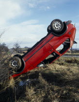 Overturned car in ditch beside country road at crash scene.