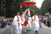 Grand procession of Toshogu shrine  1 000 man samurai procession  man in costume of Edo era high official  on horseback being lead by others in costume  one holding a parasol with crowds watching.