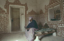 Woman in interior of traditional mud house with decorative painted design on walls.