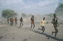 Young Dinka men carrying spears and running in line.