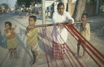 Family working together.  Two boys supporting loom for father to weave.