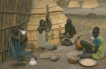 Dinka women pounding millet outside their hut.