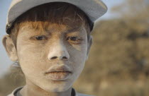 Portrait of a young boy worker with cement dust on his face  wearring a baseball cap. Banks of the Irrawaddy Myanmar