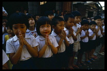 Line of school children giving traditional Thai greeting or wai with palms together and fingers extended.