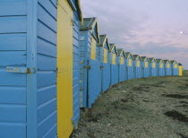 Crescent of blue and yellow beach huts in evening light with moon showing