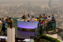 Sorocco Restaurant. People standing next to a lit up bar and looking over balcony surrounded by the Bangkok Skyline Taken from the State Tower the 2nd tallest building in Bangkok