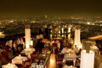 Sorocco Restaurant. People dining at tables with the Bangkok Skyline in the background.Taken from the State Tower the 2nd tallest building in Bangkok