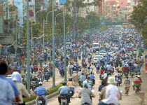 View down busy street with people riding motorbikes and bicycles